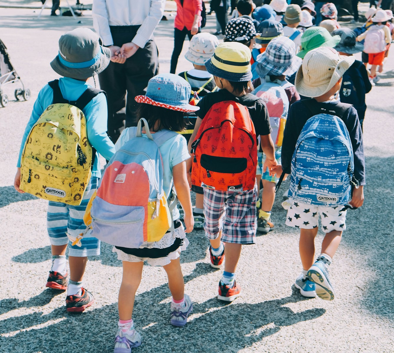 children with back-to-school insurance wearing white and orange backpacks walking on gray concrete pavement during daytime